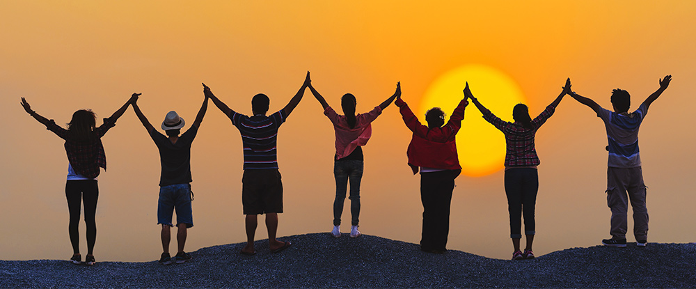 Group holding raised hands at sunset